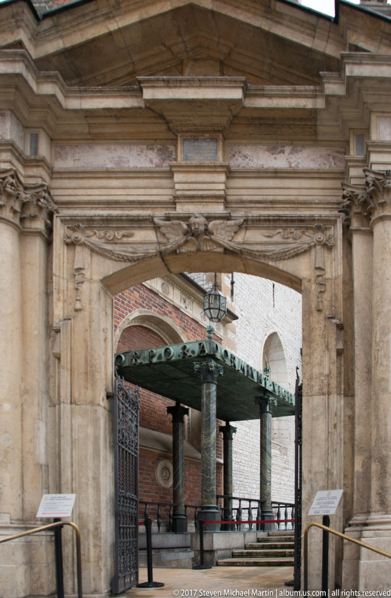 Carved stone portal with classical moldings framing a dark columned canopy in the courtyard beyond.