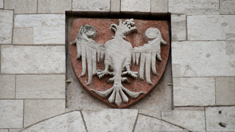 Stone shield bearing a crowned white eagle with spread wings on a pale masonry wall.