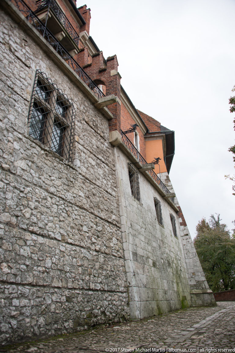 Massive sloped stone fortification wall with barred windows and red-roofed brick buildings rising above.