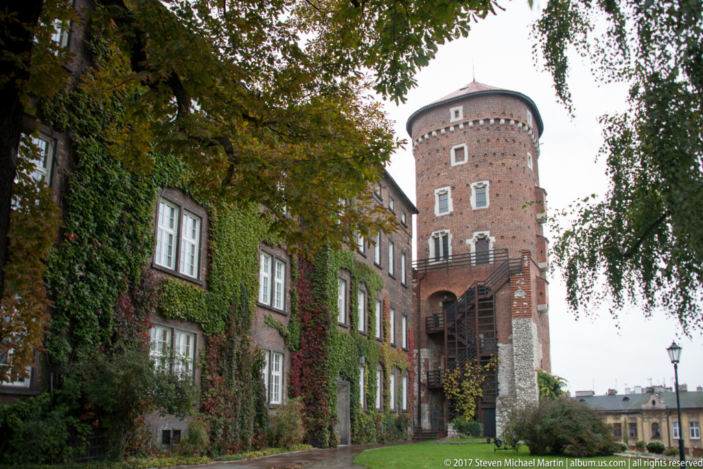 Round brick defensive tower beside an ivy-covered building with rows of white windows at Wawel Castle.