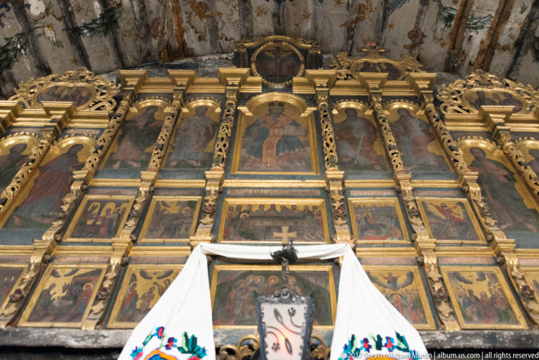 Gilded iconostasis with multiple tiers of painted icons and carved ornament inside the Wooden Church of Plopiș.
