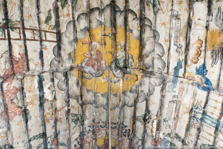 Curved wooden ceiling painted with religious figures, clouds, stars, and decorative motifs inside the Plopiș church.