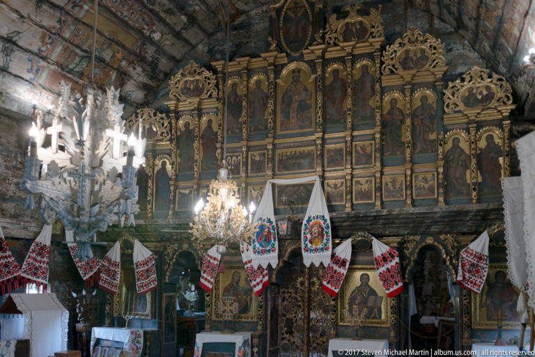 Gilded iconostasis, hanging chandeliers, and embroidered devotional cloths inside the Wooden Church of Plopiș.