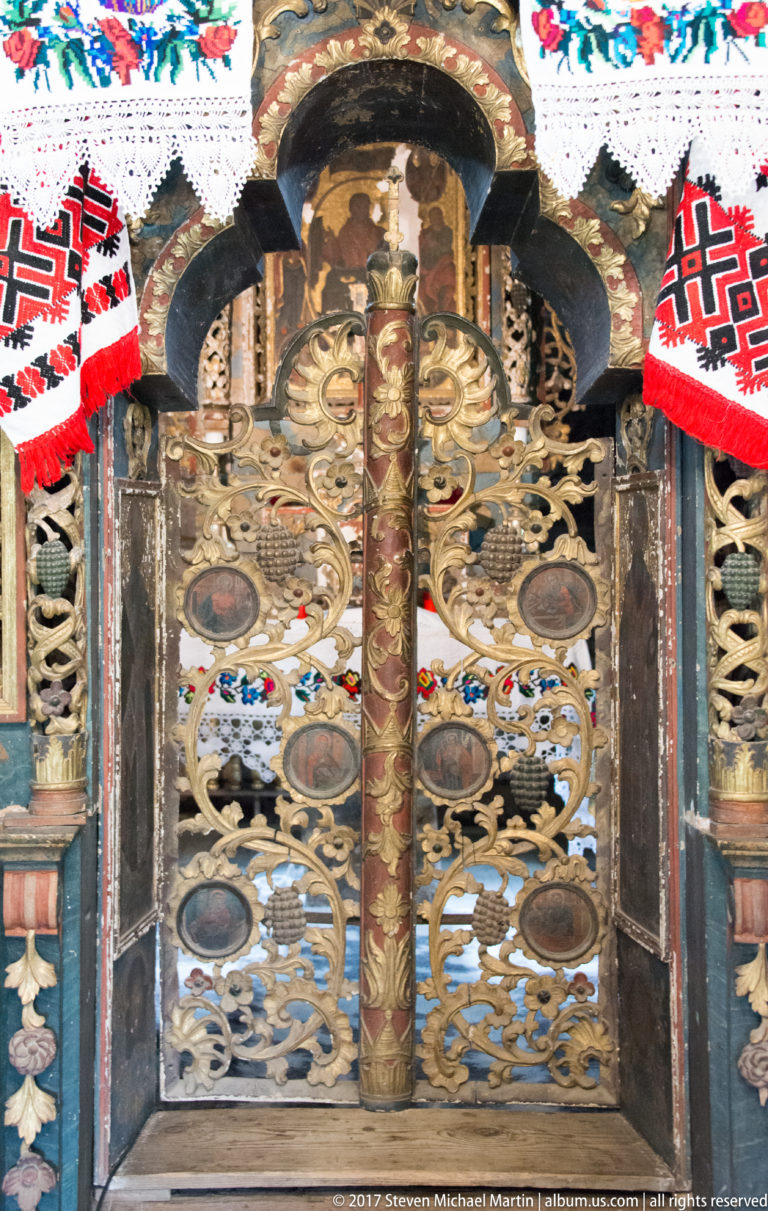 Close view of gilded carved central iconostasis doors with painted medallions and a sacred scene above.