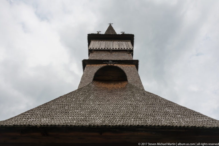 Low-angle view of the broad shingled roof rising to the tiered bell tower of the Wooden Church of Plopiș.