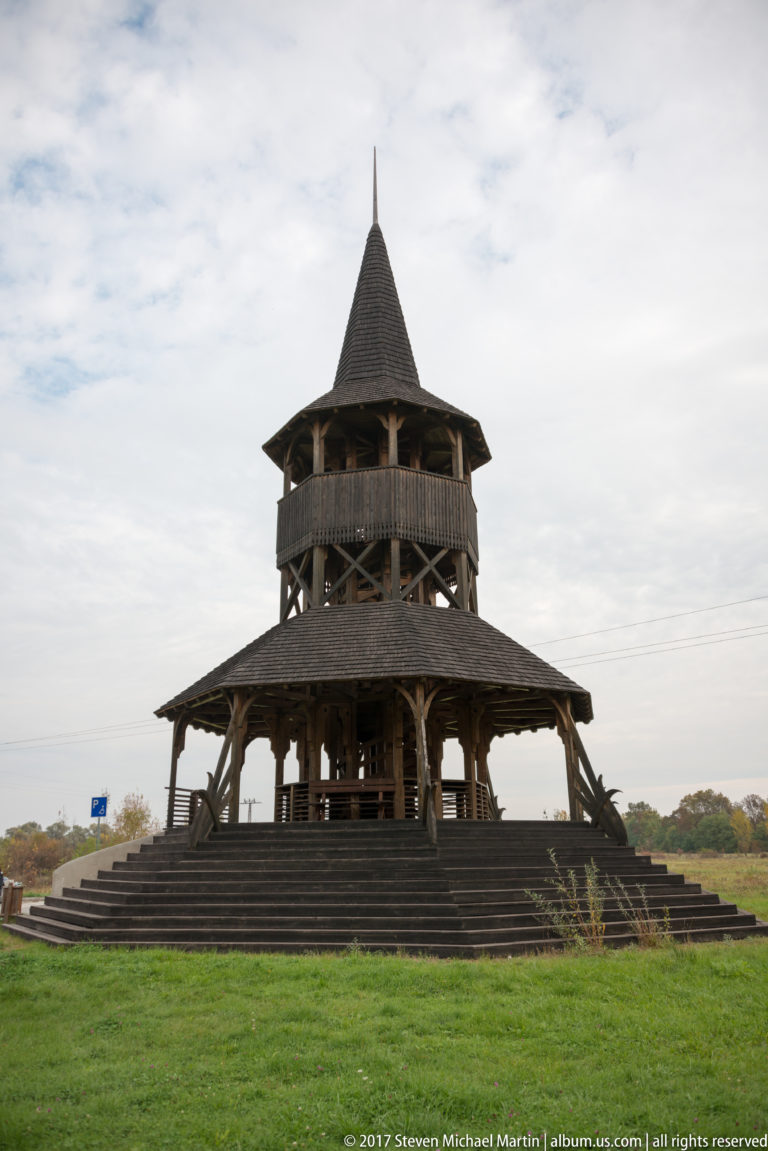 Wide view of a multi-tiered open wooden pavilion with a tall central tower, broad steps, and lawn.