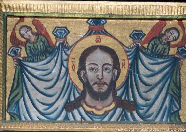 Close view of an icon showing Christ with a golden halo between two angels holding blue drapery.