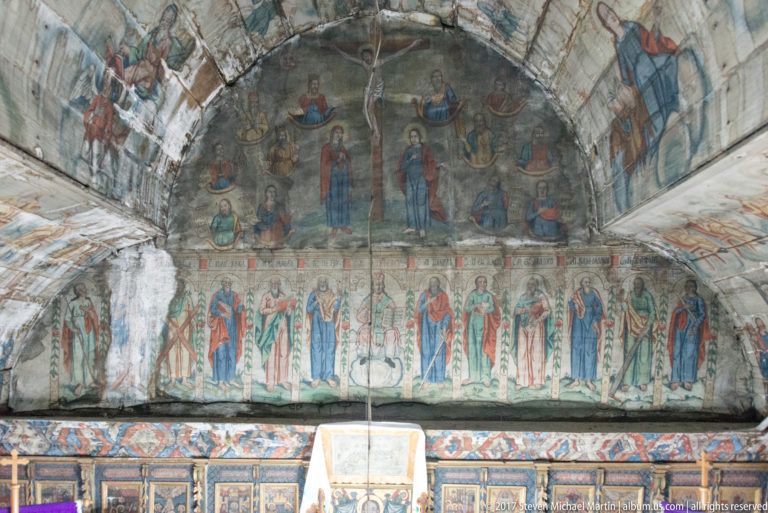 Rows of haloed saints and larger sacred figures painted across the curved upper wall of a wooden church.