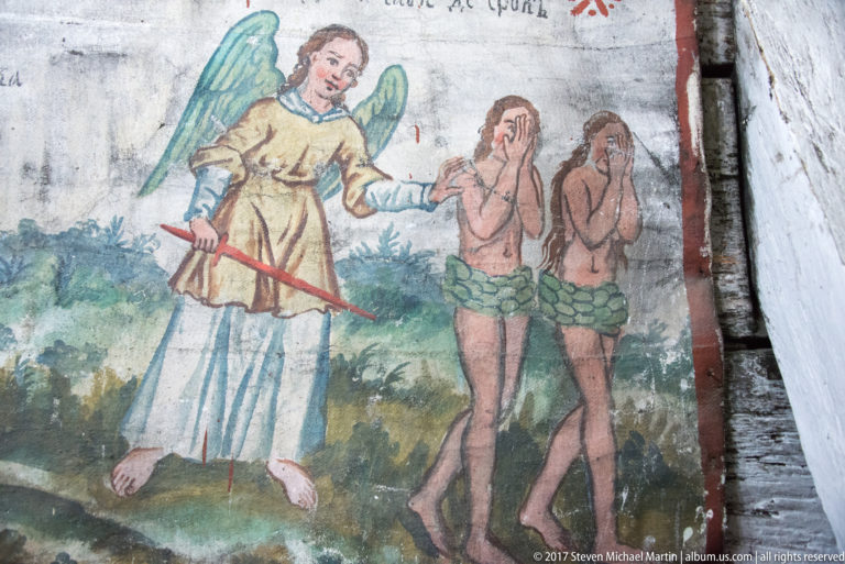 Winged angel with raised red sword driving leaf-clad Adam and Eve away in a painted biblical scene.