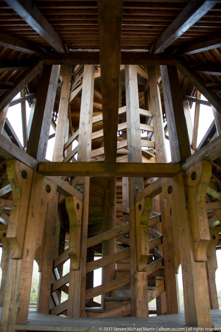 Interior structural detail of heavy wooden posts, beams, braces, and roof framing in an open pavilion.