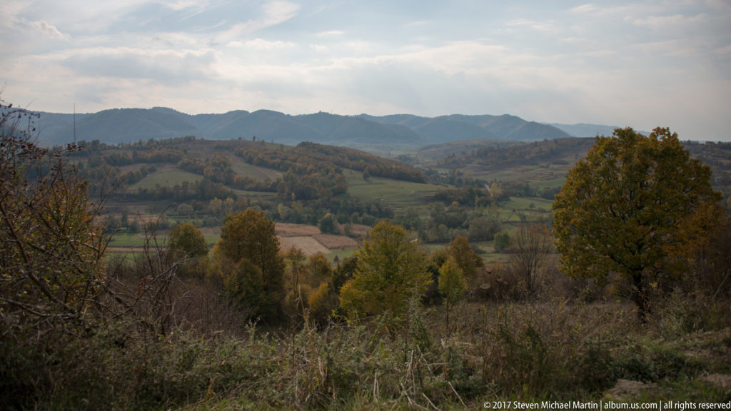 Rolling autumn fields, scattered woodland, and layered low mountain ridges across the Maramureș countryside.