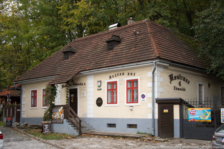 Hostinec u Zámockej building with tiled hipped roof, dormers, and red-trimmed windows.