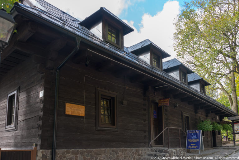 Long dark timber building with dormers, small windows, and deep eaves among trees.