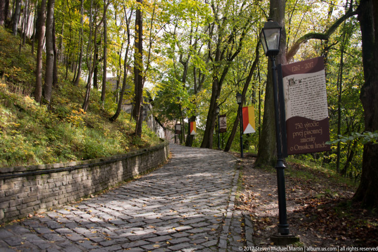 Interpretive panel beside a cobbled wooded path and route markers on the approach to Orava Castle.
