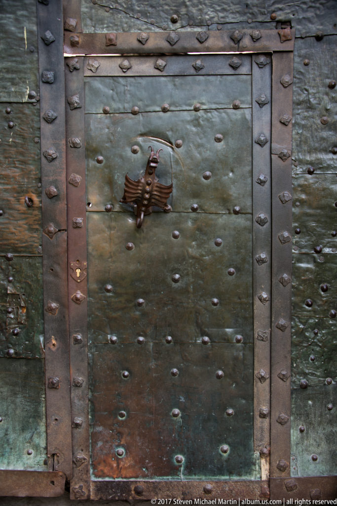Weathered riveted metal door with broad iron straps and a small central dragon-shaped fitting.