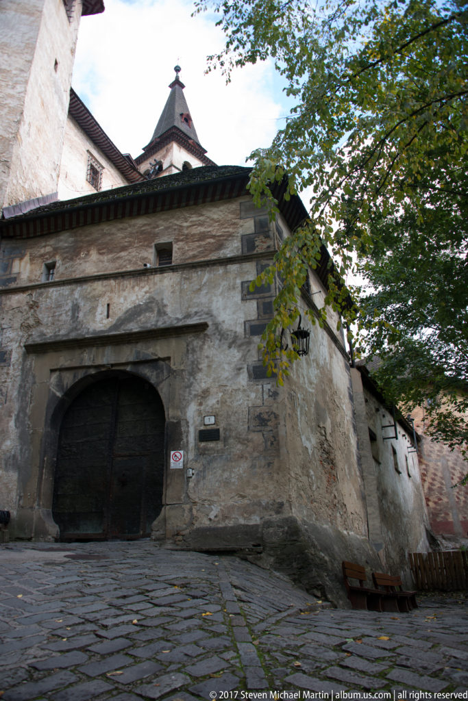 Large dark wooden double gate set in a low stone arch beside the cobbled castle approach.