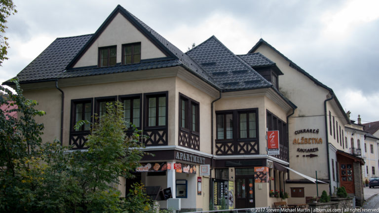 Steep-roofed commercial building with shopfronts and Cukráreň Alžbetka signage in Oravský Podzámok.