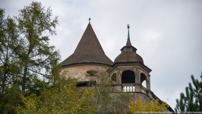 Conical-roofed round tower beside a slender spired open arcade at Orava Castle.