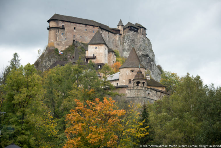 Curved wall and arcaded pavilion below the clustered towers and upper walls of Orava Castle.