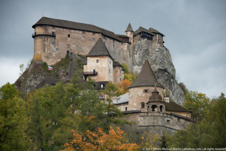 Multiple roofed towers and walls of Orava Castle stacked against a steep rocky cliff.