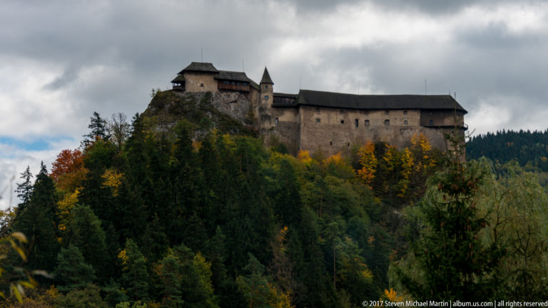Orava Castle extending along a wooded rocky summit beneath cloudy skies in autumn.