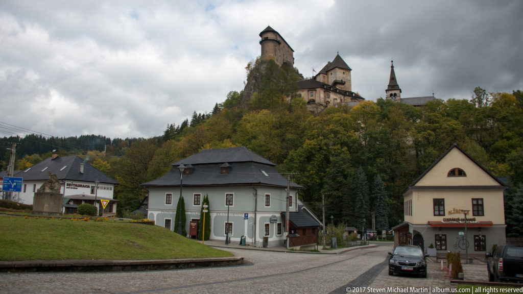 Village buildings and road in Oravský Podzámok below Orava Castle on a wooded ridge.
