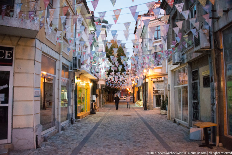 Narrow cobbled pedestrian lane with illuminated shopfronts and dense rows of triangular bunting overhead.