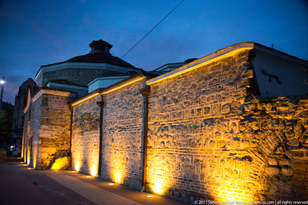 Long historic stone wall illuminated from below along a quiet Plovdiv street at blue hour.