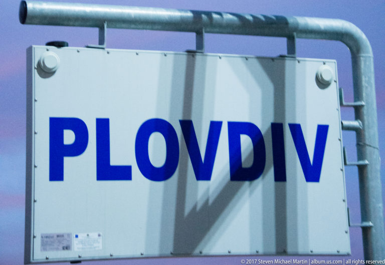 White rectangular sign with large blue capital letters spelling PLOVDIV inside a galvanized metal frame.
