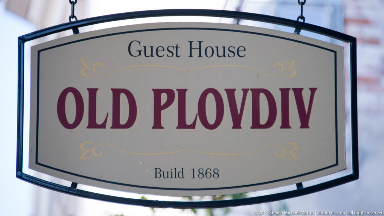 Hanging cream sign reading “Guest House OLD PLOVDIV” and “Build 1868” in burgundy and black lettering.