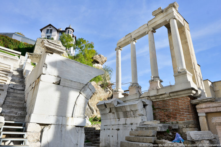Three tall stone columns above block masonry, brickwork, steps, and rock at Plovdiv’s ancient theatre.