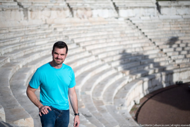 Man in a turquoise shirt standing before curved pale stone seating inside Plovdiv’s ancient Roman theatre.