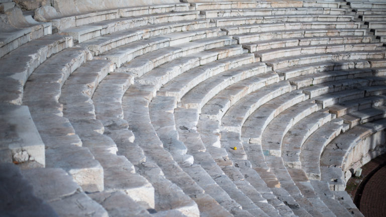 Curving tiers of pale stone seats descend toward the lower right, their worn edges highlighted by side light.