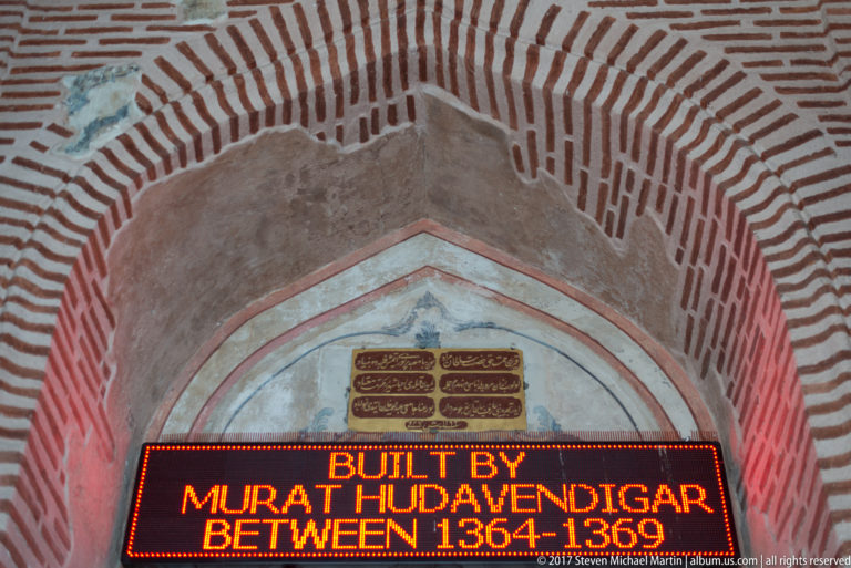 Pointed brick arch above Arabic-script plaques and an illuminated English sign giving a 1364–1369 construction date.