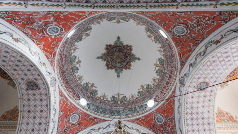 Upward view of a painted circular medallion surrounded by floral sprays, patterned borders, and smaller roundels.