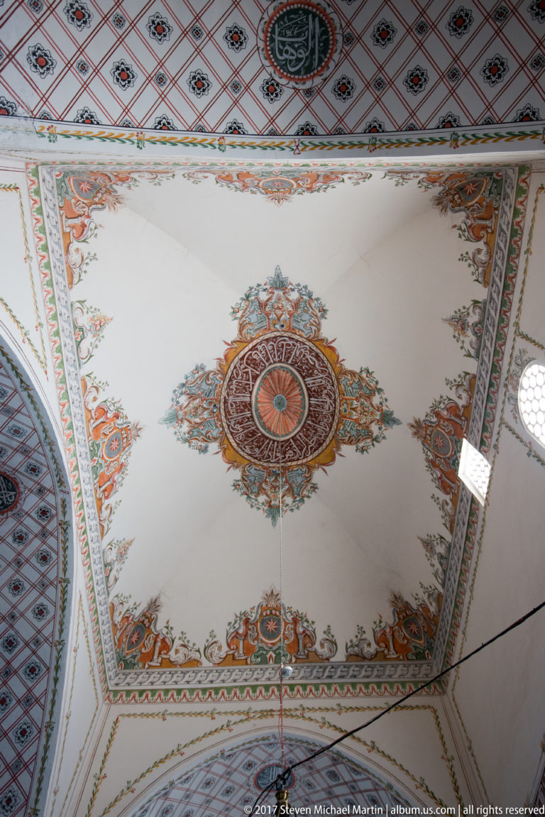 Rectangular mosque ceiling panel with central painted rosette, floral corner ornament, and patterned border bands.