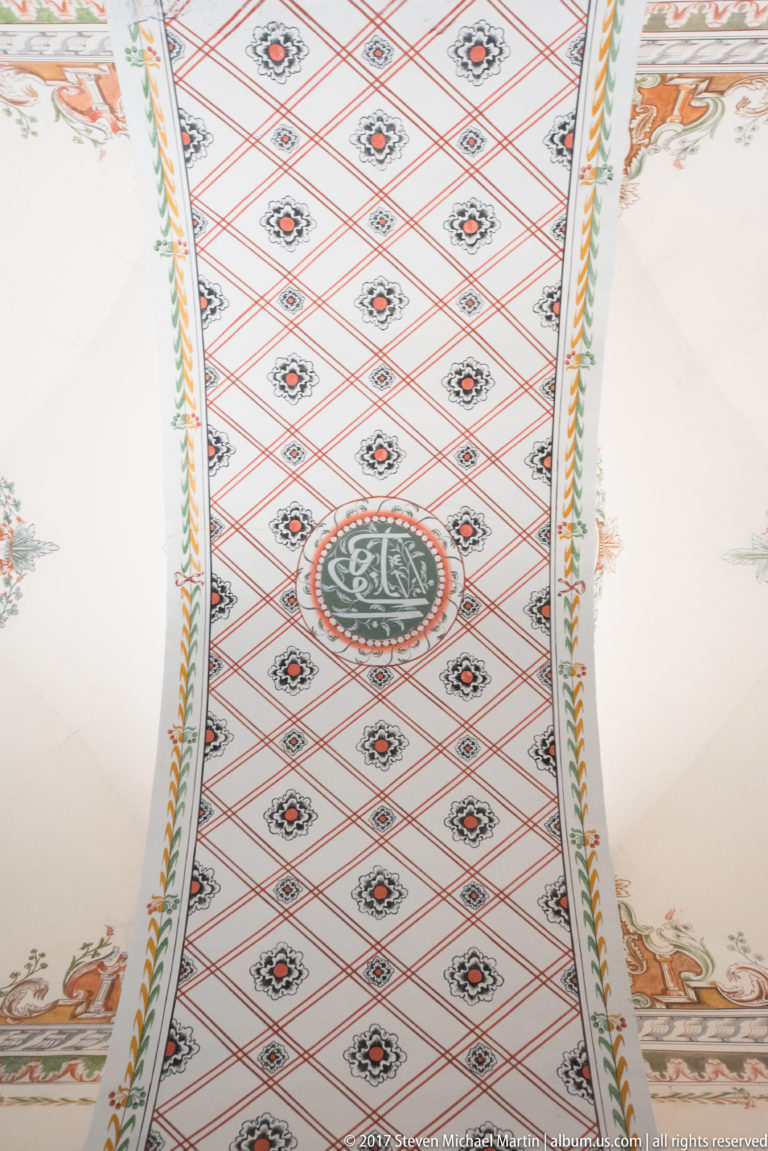 Diamond-patterned mosque vault with small rosettes and a central dark circular medallion containing Arabic calligraphy.