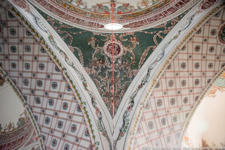 Painted green triangular vault field with floral scrollwork meeting red-and-gray geometric ceiling patterns along white ribs.
