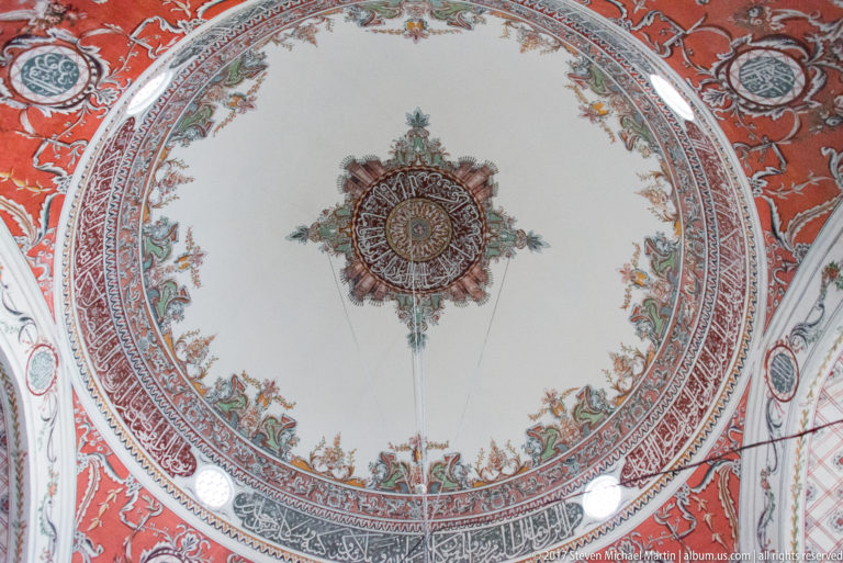 Large circular ceiling design with central rosette, concentric patterned bands, floral motifs, and red surrounding vault surfaces.