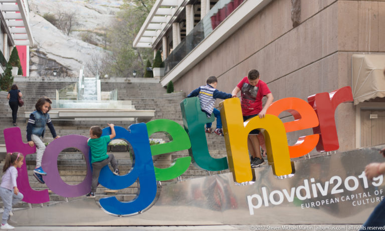 Children climbing colorful oversized “together” letters beside Plovdiv 2019 European Capital of Culture branding.