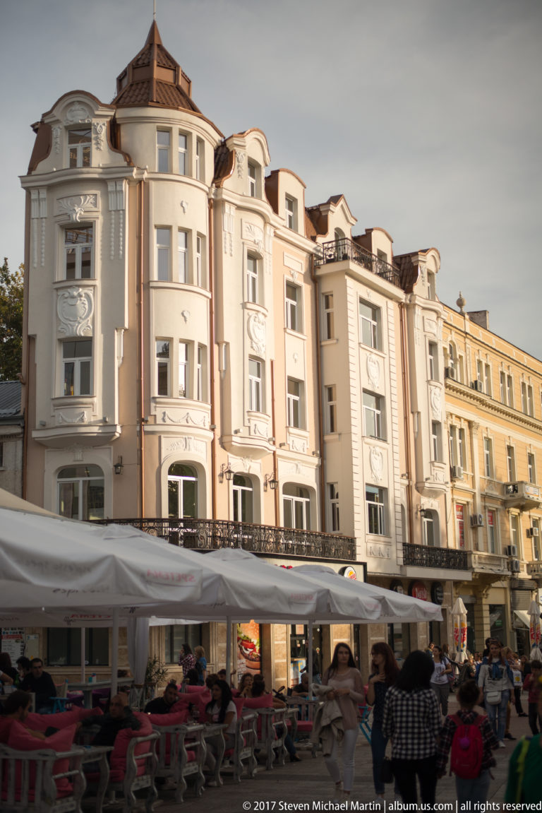 Ornate cream and pastel historic façades rising above crowded outdoor café tables in central Plovdiv.