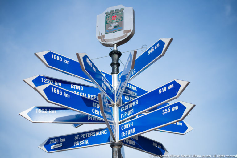 Blue multi-directional signpost beneath the Plovdiv crest, with city names and kilometer distances in Latin and Cyrillic scripts.