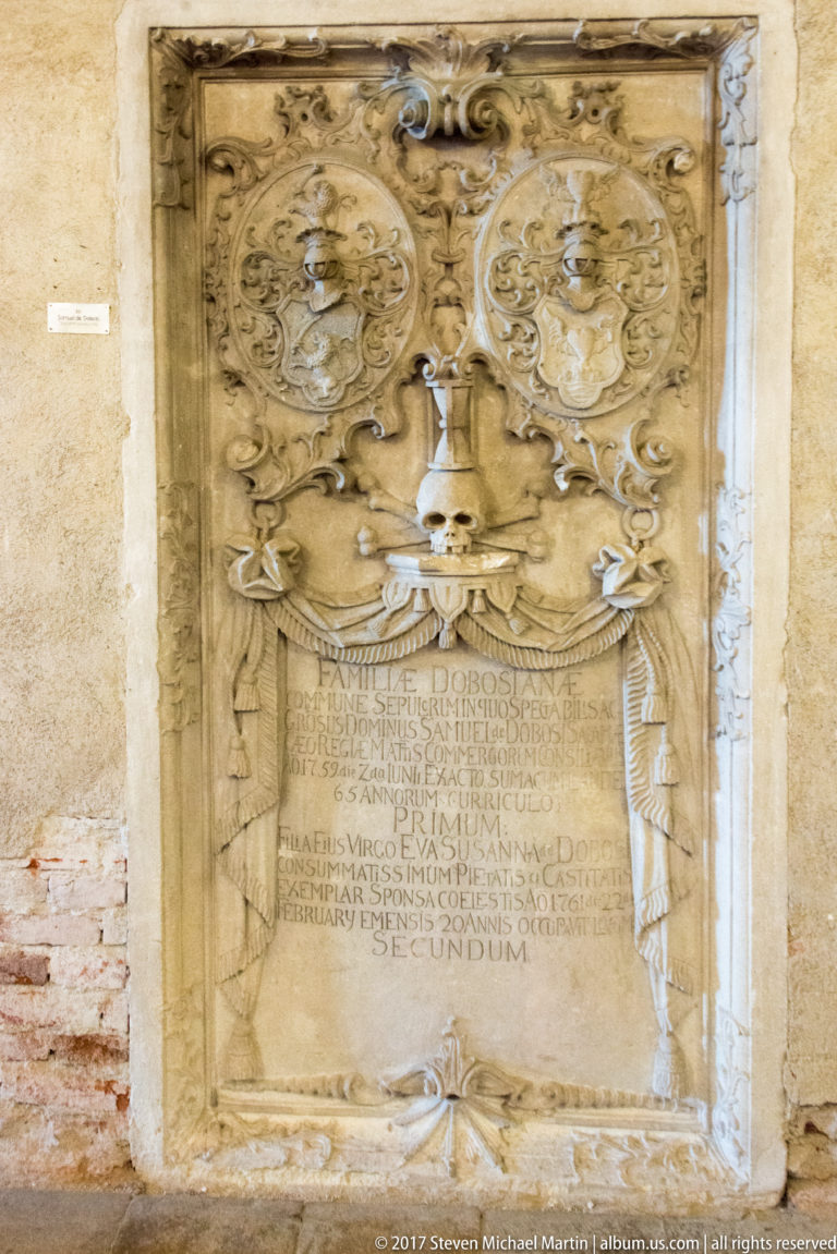 Ornate stone epitaph with inscription panel, scrollwork, heraldic motifs, and skeletal figures on either side.