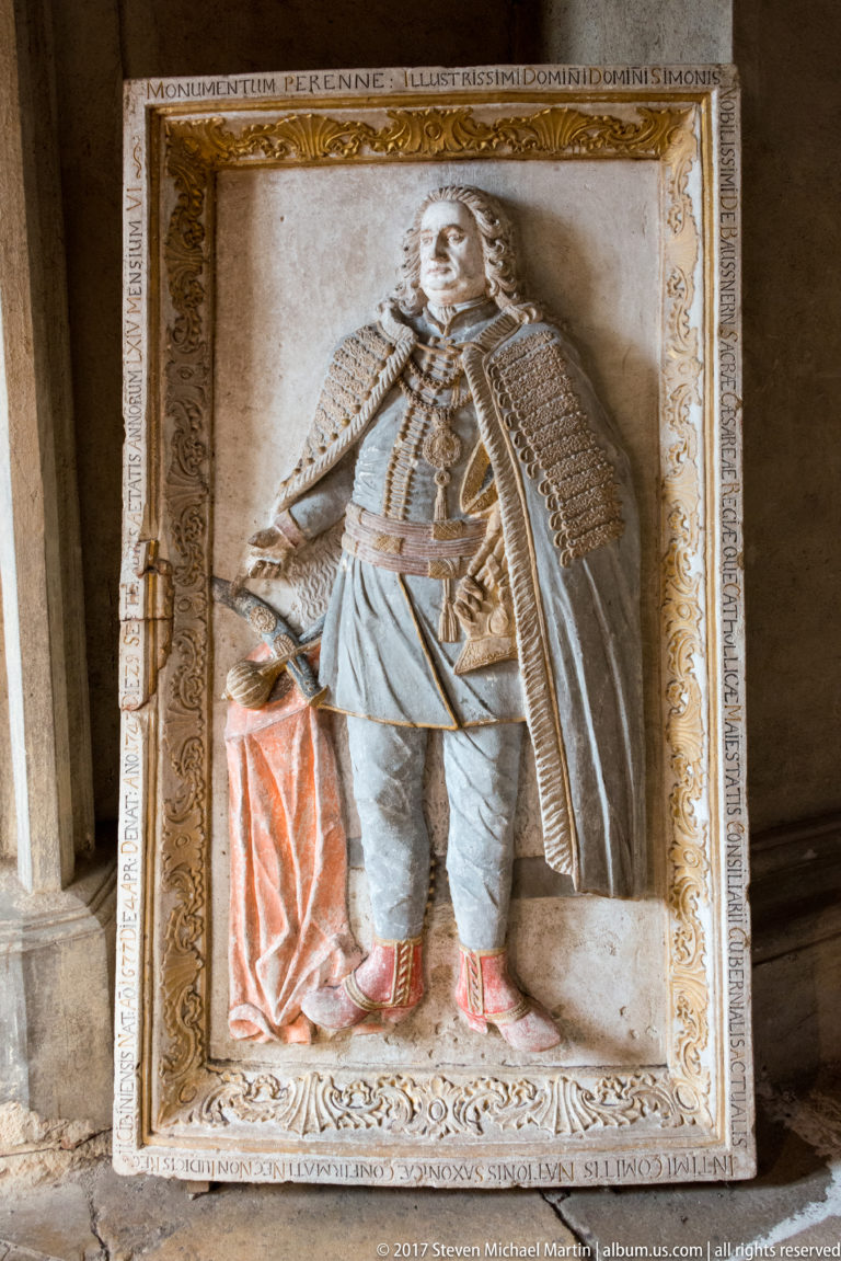 Carved funerary relief of a standing nobleman in ornate historic dress within an inscribed rectangular frame.