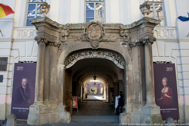 Ornately carved stone portal leading through a vaulted passage, with historical portrait banners on both sides.