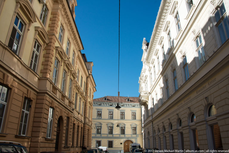 Narrow Sibiu street lined by tall ocher and pale historic façades with rows of windows beneath a vivid blue sky.