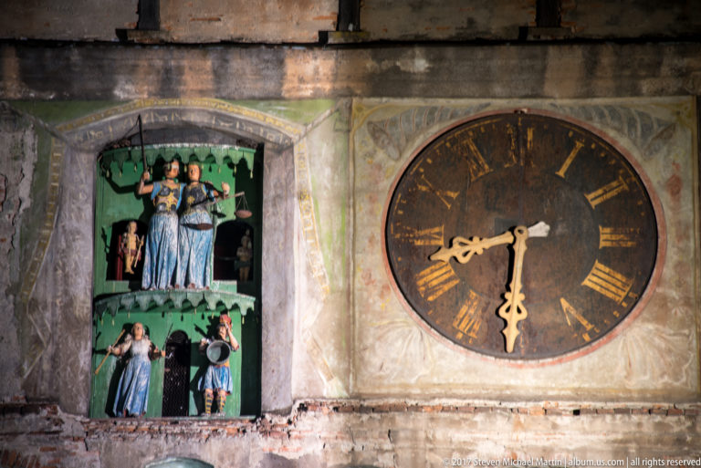 Large Roman-numeral clock face beside brightly painted automaton figures in Sighisoara's Clock Tower.