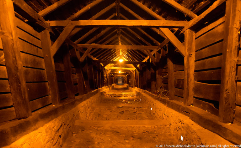 Warmly lit interior of the covered Scholars' Stairs, with timber trusses and steep steps receding uphill.