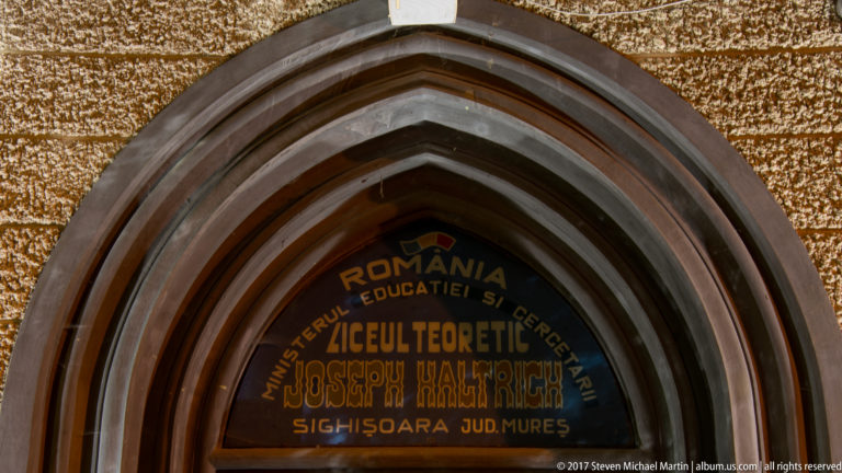 Pointed-arch entrance panel reading “Liceul Teoretic Joseph Haltrich” and “Sighisoara Jud. Mures.”