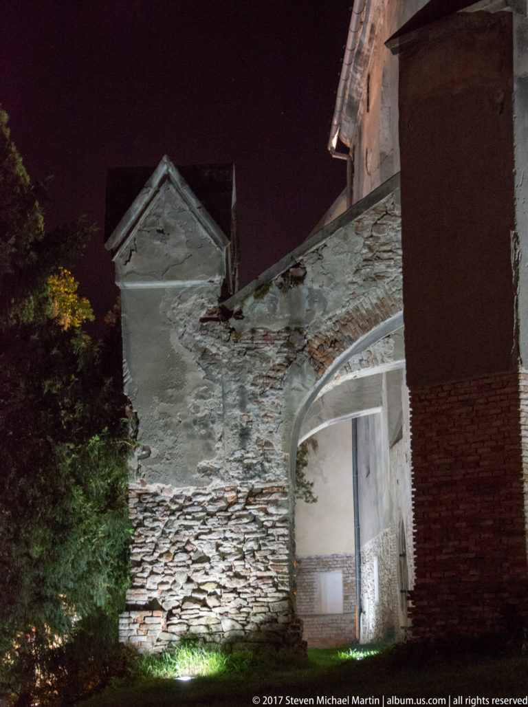 Night-lit cluster of rough stone and plaster buildings with a small gabled projection.
